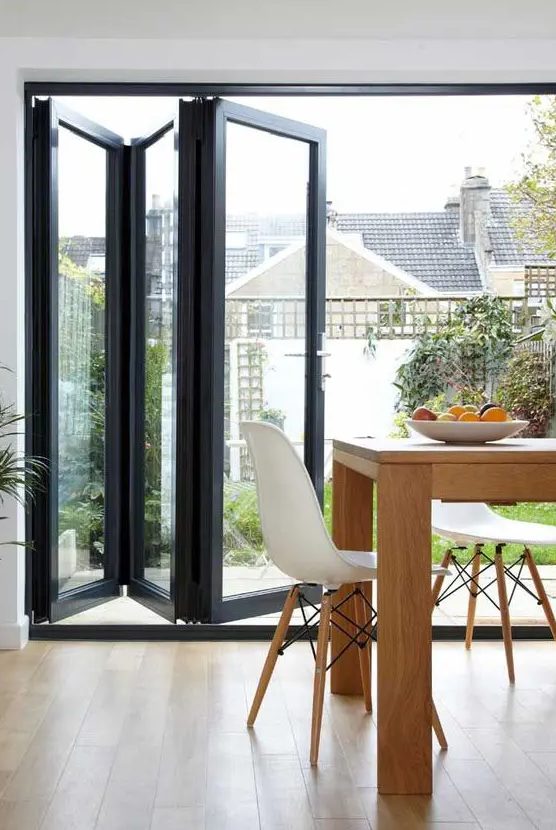 a black frame glass folding door separates the dining room from the garden and lets enjoy the views and natural light and lets an easy access to the garden
