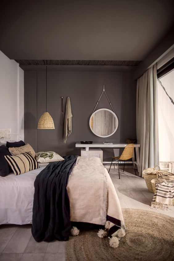 a bold bedroom with a taupe ceiling and accent wall, a white desk and a bed with contrasting bedding, a jute rug and pendant lamps