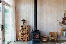 a cabin space fully clad with wood, with a wood burning stove and some firewood in crates for a cozy feel