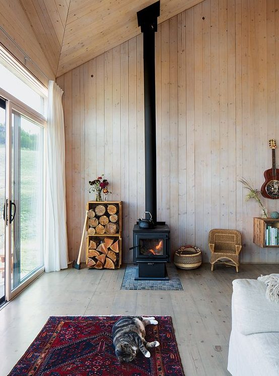 a cabin space fully clad with wood, with a wood burning stove and some firewood in crates for a cozy feel