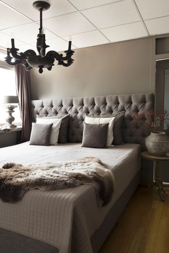 a catchy taupe bedroom with a brown upholstered bed, a black vintage chandelier and round nightstands