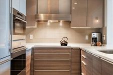 a chic stained kitchen with matching glossy taupe cabinets, white stone countertops and a tan tile backsplash