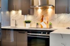 a chic taupe kitchen with glossy cabinets, a white marble tile backsplash and countertops, built-in appliances is a bold idea to try