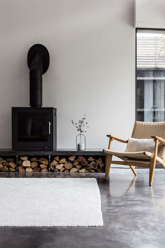a contemporary space with a wood burning stove and firewood storage of concrete, a stylish chair and a white rug