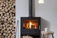 a contemproary space with a Nordic feel is cozied up with a modern wood burning stove and some firewood stored right here