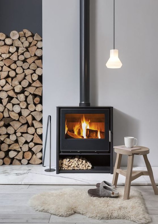 a contemproary space with a Nordic feel is cozied up with a modern wood burning stove and some firewood stored right here