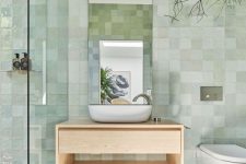 a dreamy and airy bathroom with green Zellige tiles on the walls, grey tiles on the floor, a floating vanity and an arched mirror