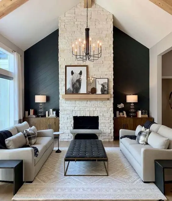 a farmhouse living room with a black shiplap accent wall, a fireplace clad with faux stone, grey sofas, a black leather ottoman