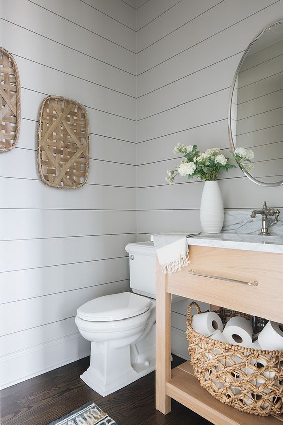 a fresh farmhouse bathroom with off white shiplap, a wooden vanity, decorative baskets and touches of white