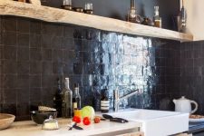 a light-stained kitchen with a black Zellige tile backsplash, an open shelf and a white sink plus black bulbs hanging