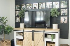 a living room with a black shiplap accent wall, a farmhouse TV unit, a cool gallery wall with family pics