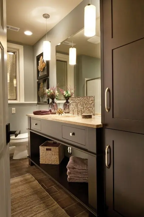 a long and narrow bathroom with elegant taupe cabinetry, grey walls and a tiled floor plus chic pendant lamps