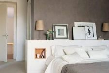 a lovely modern bedroom with a taupe accent wall, a white bed with a storage headboard, artworks and lamps and white bedding