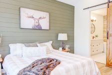 a lovely woodland bedroom with a green shiplap accent wall, wooden nightstands with lamps, a moose artwork and a bed with checked bedding