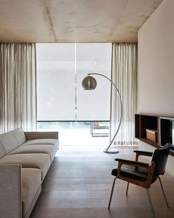 a minimalist neutral space with blinds and neutral semi-sheer curtains that block sunshine and add interest to the space