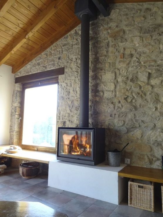 a modern rustic space with stone walls and a wooden ceiling plus a super modern and sleek wood burning stove