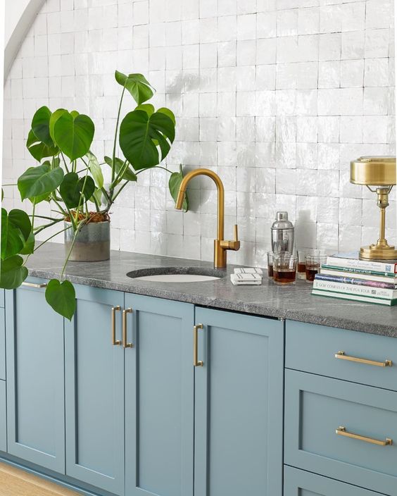 a modern stone blue kitchen with shaker style cabinets and grey stone countertops, gold fixtures and a potted plant is amazing