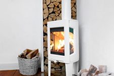 a modern white wood burning stove on a glass stand, with firewood in the corner and baskets for firewood