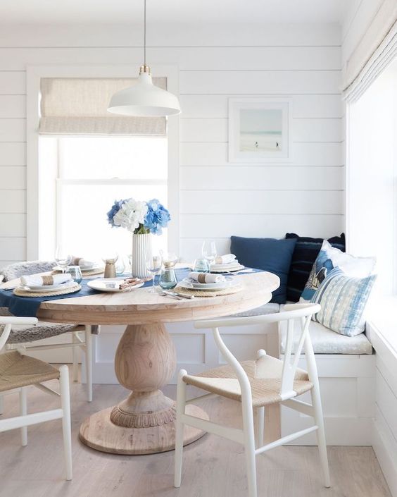 a nautical breakfast nook with wishbone chairs, white shiplap walls and a round vintage dining table