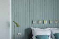 a peaceful Nordic bedroom with a pastel green shiplap wall, a grey bed with green bedding, a black nightstand