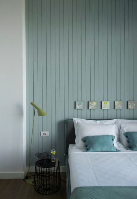 a peaceful Nordic bedroom with a pastel green shiplap wall, a grey bed with green bedding, a black nightstand