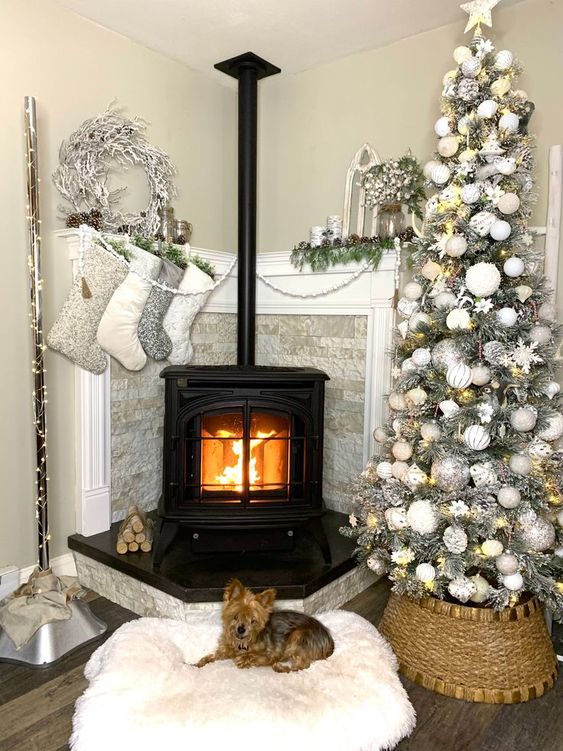 a pretty Christmas styled nook with a hearth, stockings, greenery, a white wreath and a gorgeous silver Christmas tree with lights
