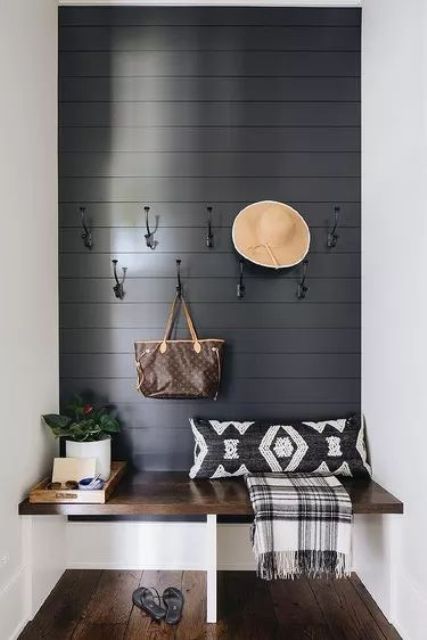 a pretty boho entryway with a black shiplap accent wall, a bench, printed pillows, hooks and a potted plant