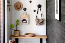 a pretty entryway with white and black shiplap walls, a wooden bench, round hooks on the wall and a plant