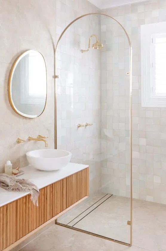a refined bathroom clad with neutral and pastel Zellige tiles in the shower, with a curved space divider and a floating wooden vanity