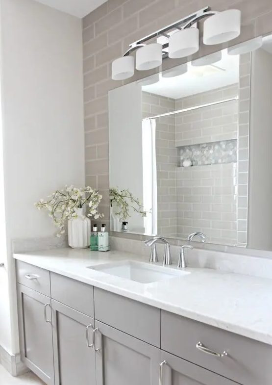 a refined bathroom with skinny taupe tiles, a taupe vanity, a white countertop, an oversized mirror and a large sconce is a pretty idea