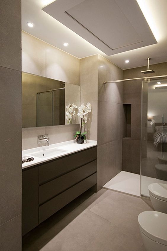 a refined minimalist bathroom with tan walls and a floor, a lit up ceiling, a taupe vanity, white appliances and a large mirror