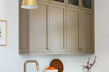 a refined taupe kitchen with shaker cabinets – mostly lower and a couple of upper ones, white stone countertops and a backsplash, gold pendant lamps