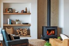 a small and cozy living room with a hearth, grey and amber sitting furniture, niche shelves and firewood in the stand