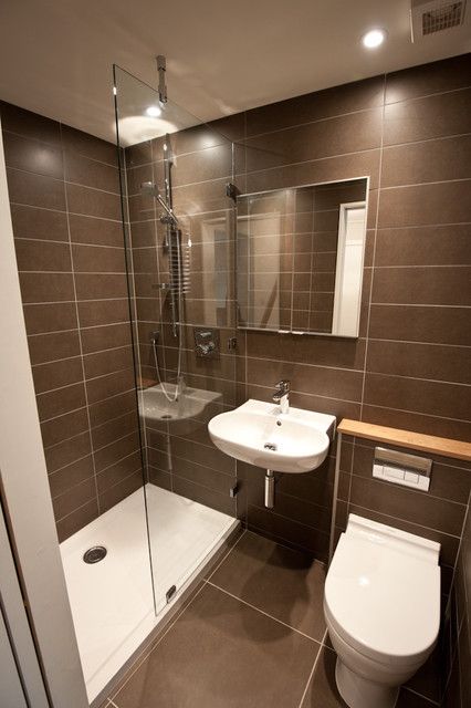 a small and stylish modern taupe bathroom with skinny tiles, white appliances and built in lights and a shower space