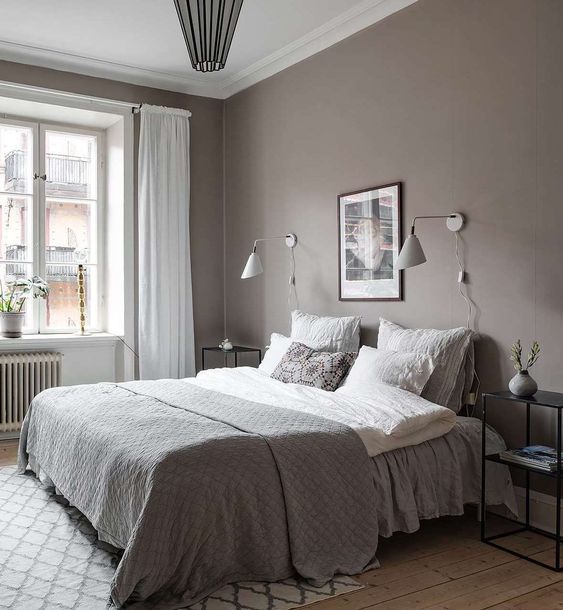 a stylish Scandi bedroom with taupe walls, a bed with white and grey bedding, black nightstands and white sonces