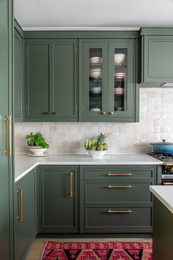 a stylish green kitchen with shaker style cabinets, white stone countertops, a neutral Zellige tile backsplash and gold fixtures