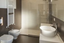 a stylish modern bathroom clad with neutral and taupe tiles, with a white floating vanity and white appliances