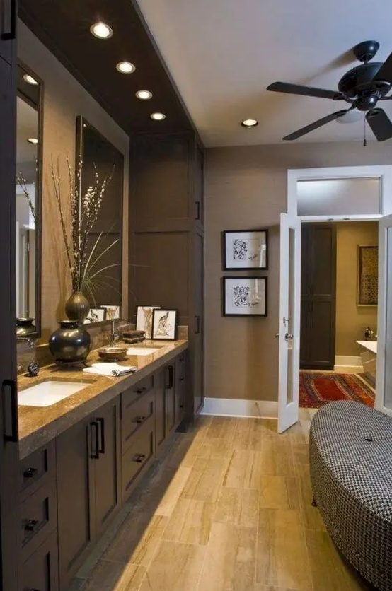 a taupe bathroom with a dark double vanity, built-in sinks and lights, an upholstered bench and blooms is very chic