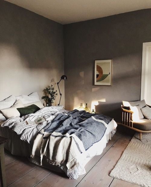 a taupe bedroom with a neutral bed and a cozy modern chair, neutral bedding and pillows, a black lamp and an artwork