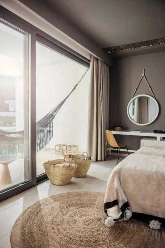 a taupe bedroom with an upholstered bed, a console taht doubles as a vanity, a round mirror and a hammock in the balcony