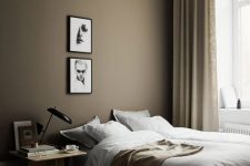 a taupe bedroom with molding on the ceiling, a bed with neutral bedding, a wooden nightstand and a black lamp, a mini gallery wall