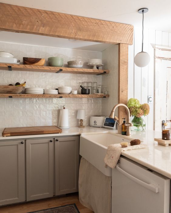 a taupe kitchen with open shelves instead of upper cabinets, white tiles on the backsplash and a vintage sink plus wooden beams