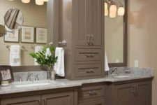 a vintage farmhouse bathroom with taupe cabinetry, stone countertops, creative sconces and stainless steel fixtures