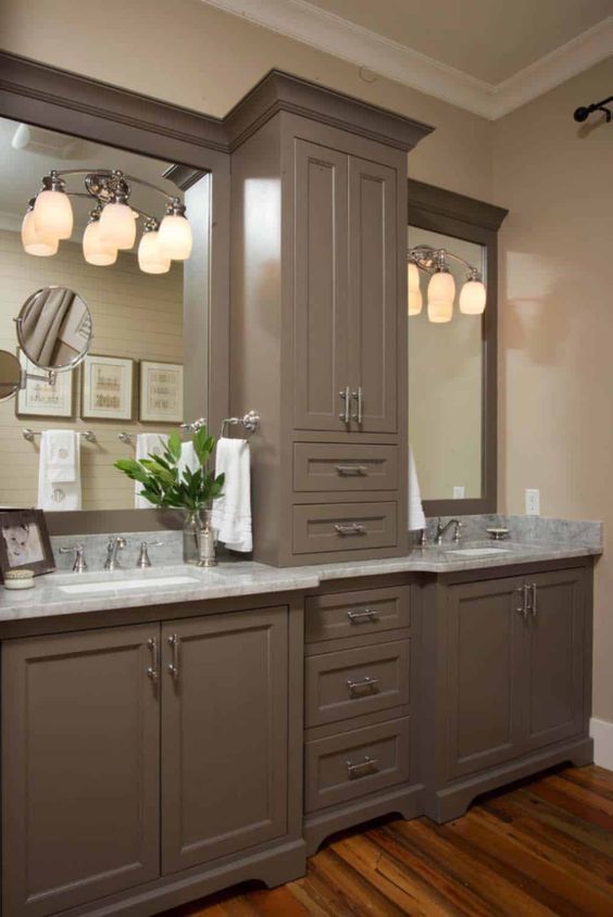 a vintage farmhouse bathroom with taupe cabinetry, stone countertops, creative sconces and stainless steel fixtures