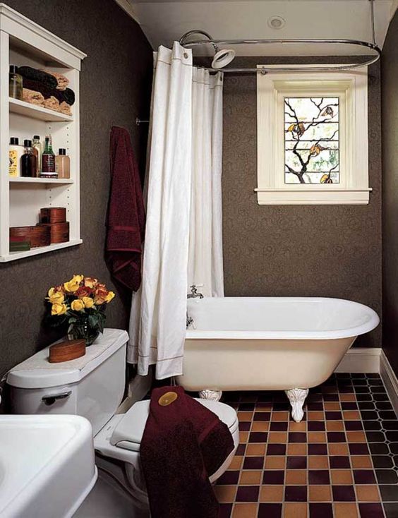 a vintage inspired taupe bathroom with a white clawfoot tub, white appliances a small mosaic window and burgundy towels
