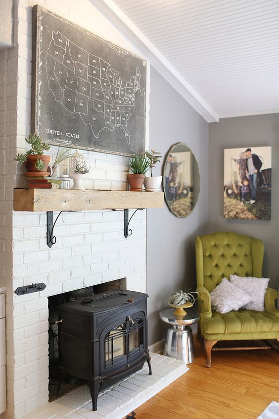 a vintage living room with a black hearth surrounded with white brick, a green chair, chic artworks and potted plants is all cool