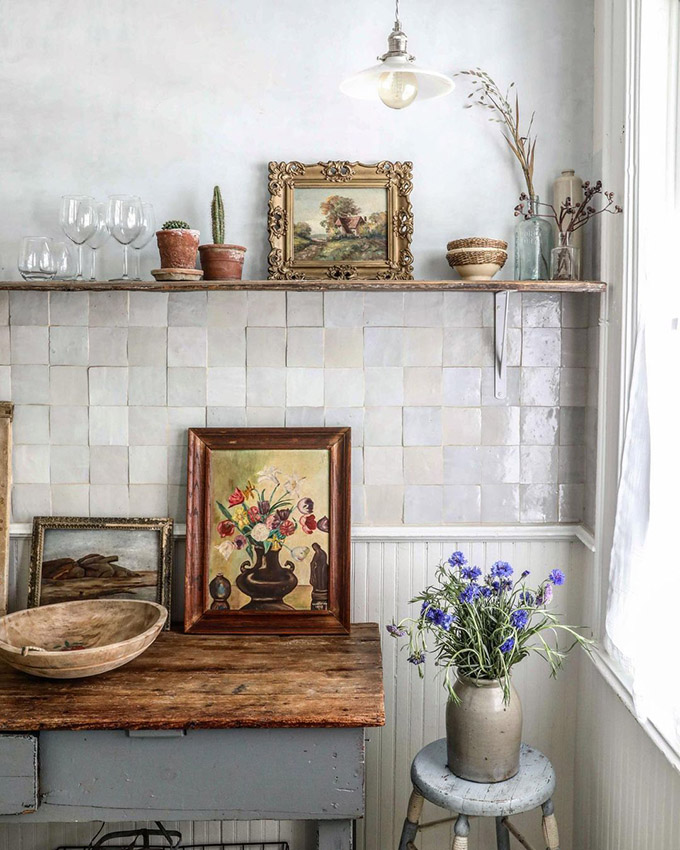 a vintage space with white wainscoting and neutral Zellige tiles, a reclaimed wood kitchen island and an open shelf, some art and blooms