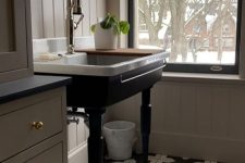 a vintage taupe bathroom with shiplap walls, vintage cabinetry, a black vanity with a vintage sink and a potted plant