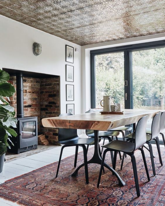 a welcoming modern dinign room with a glazed wall, a wood burning stove, a boho rug and a living edge table, chic chairs