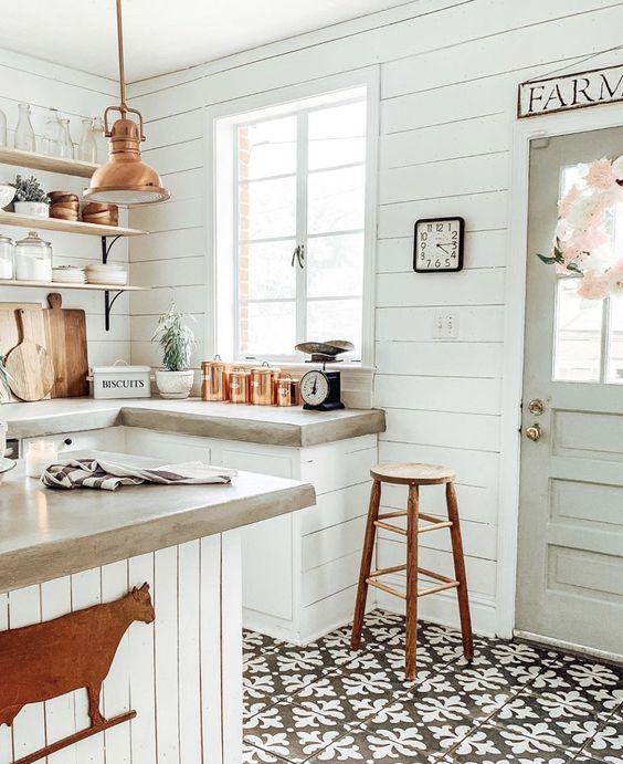 a white famrhouse kitchen clad with shiplap and shiplap cabinets, concrete countertops, a copper pendant lamp and a tall stool